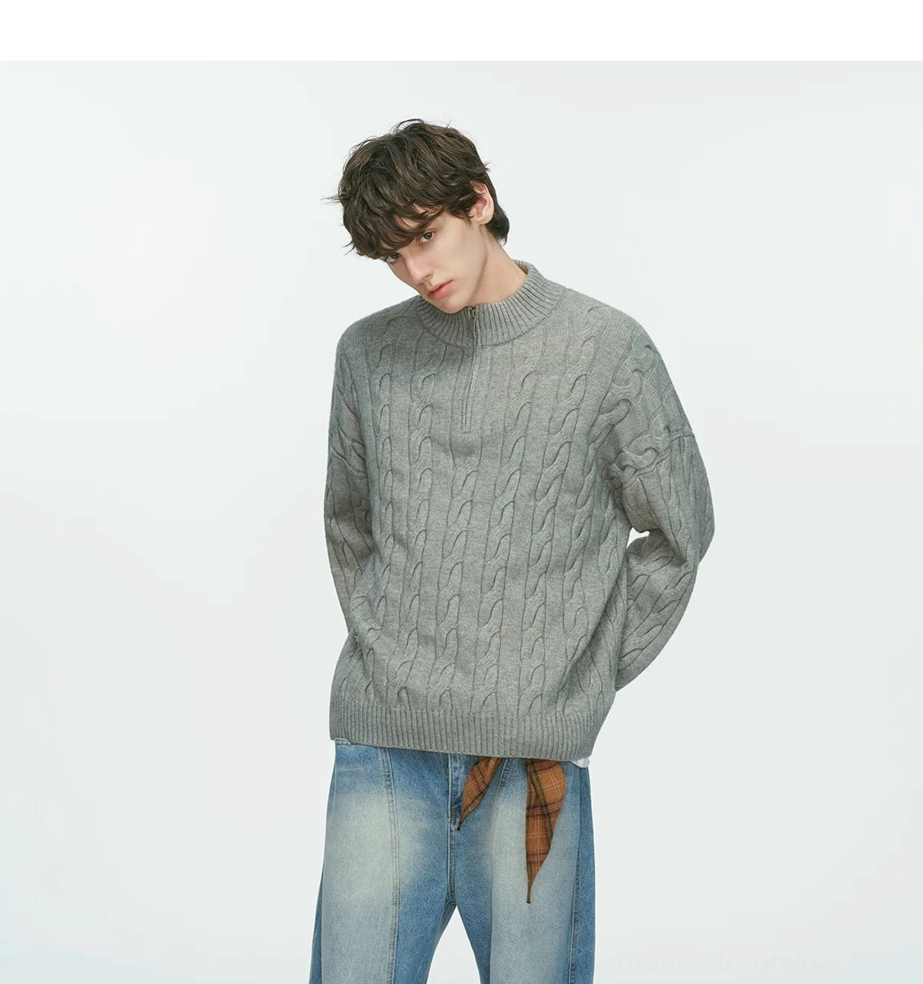 Three-quarter view of a grey oversized cable-knit half-zip sweater with hands in pockets, light wash jeans and plaid scarf