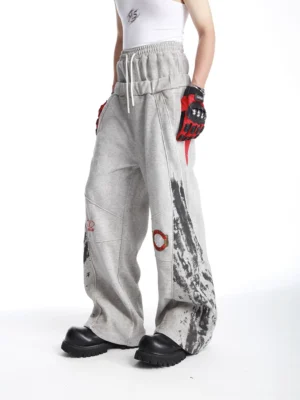 Grey oversized graphic sweatpants three-quarter side view showing black splatter print and red hip accent panel