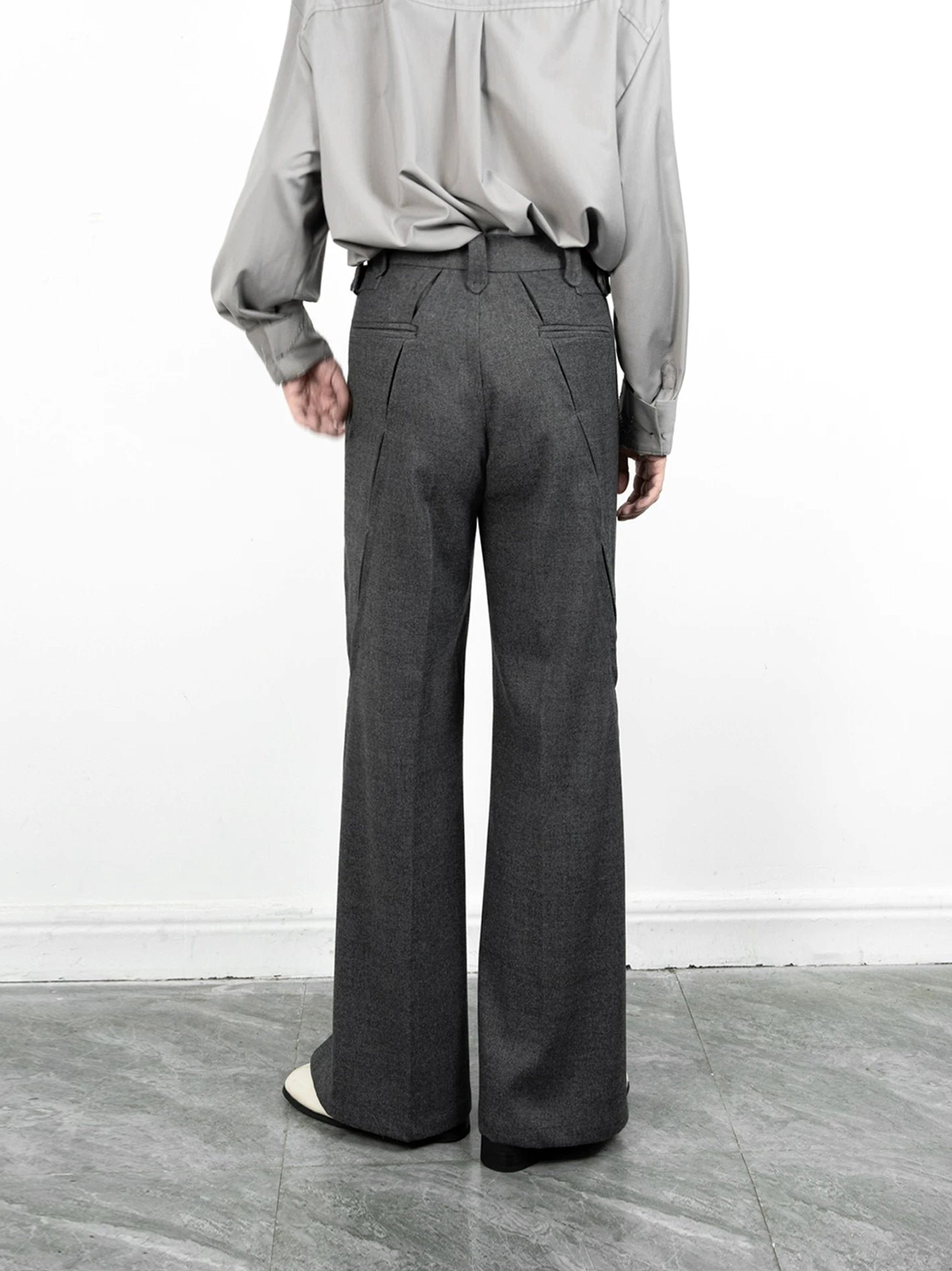Back view of grey split-hem wide-leg streetwear trousers with belt loops, welt pockets, and side hem slits styled with a light grey shirt