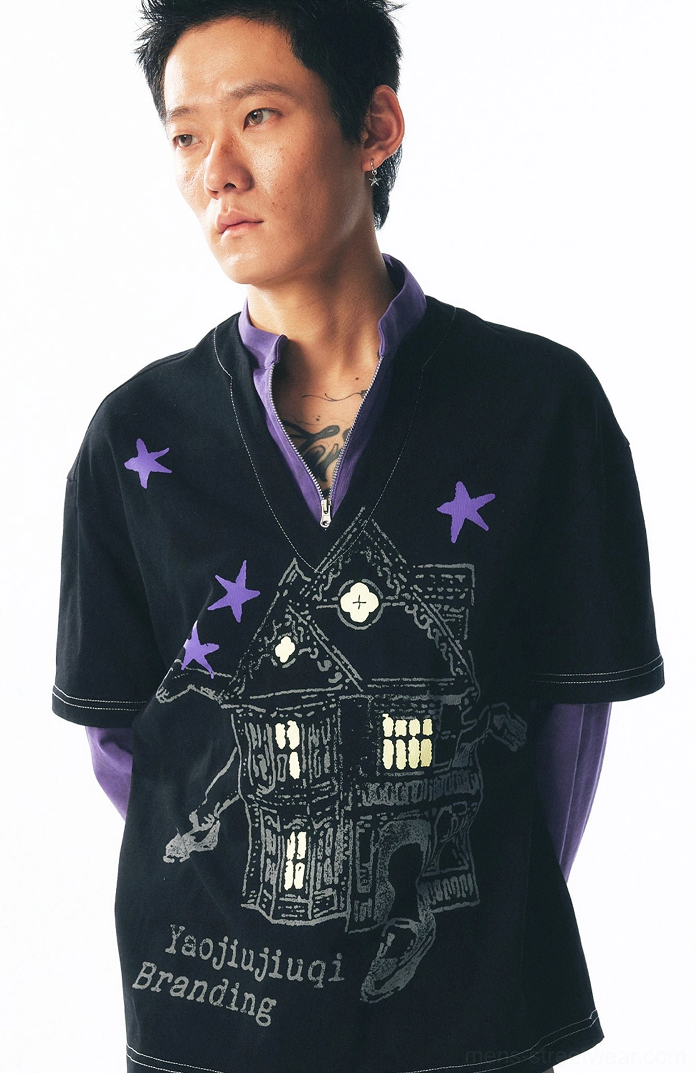 Side front detail of a black and purple layered streetwear tee showing the half-zip collar, haunted house print, and contrast stitching