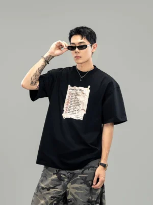 Front view of oversized black streetwear graphic T-shirt with torn paper checklist print silver necklaces sunglasses and relaxed fit