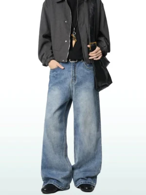 Male model wearing medium blue washed wide-leg jeans with a black tee, cropped dark gray jacket, and leather shoulder bag in a Korean streetwear outfit