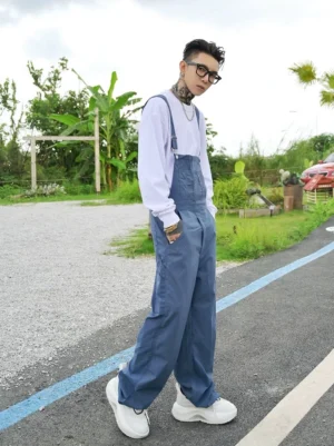 Side view of relaxed Haze Blue wide-leg utility overalls with adjustable straps worn over a white long-sleeve shirt