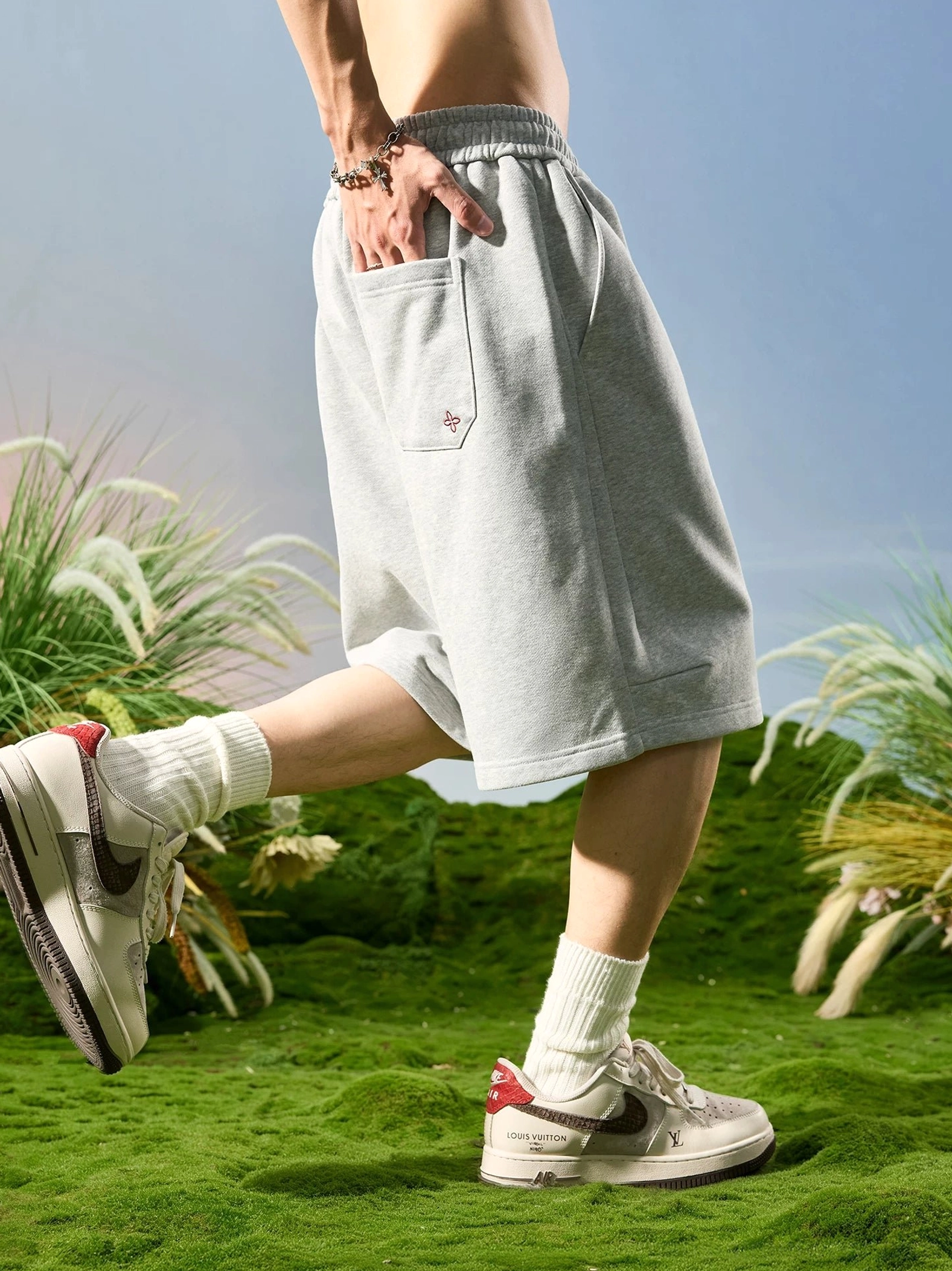 Heather ash relaxed wide-leg fleece shorts shown from a low rear angle with elastic drawstring waistband and back patch pocket on a male model
