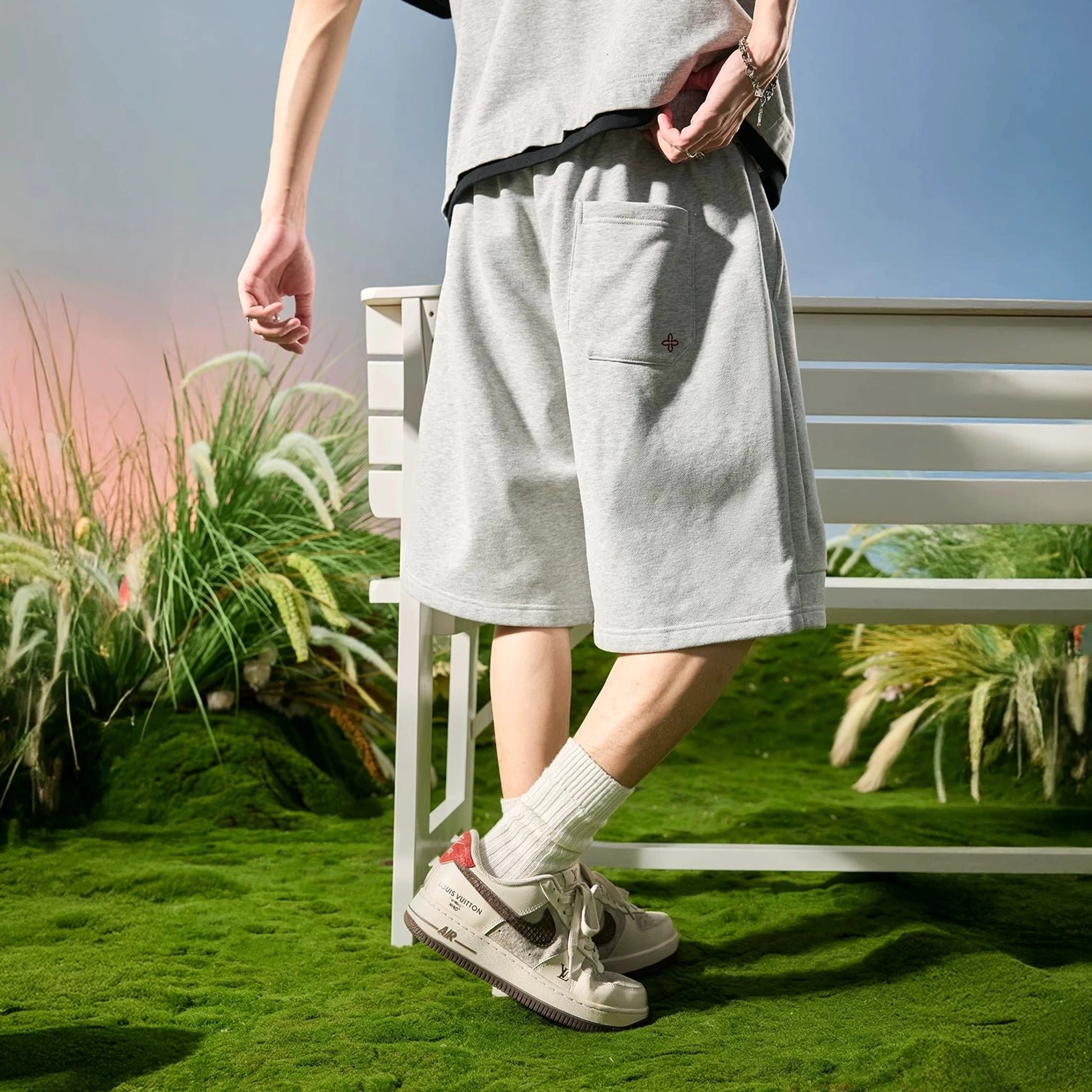 Heather ash wide-leg cloud fleece shorts shown from the rear side near a park bench with a relaxed cropped tee and casual sneakers