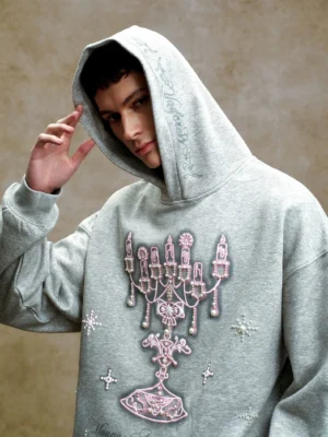 Close-up three-quarter view of heather gray oversized hoodie with pink chandelier embroidery pearl-like studs and hood script detail