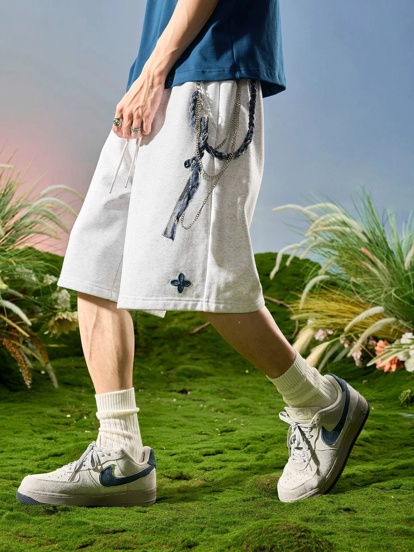 Heather light gray relaxed sweat shorts with dark clover embroidery, twisted rope drawstring, and loose leg opening styled in contemporary Asian streetwear