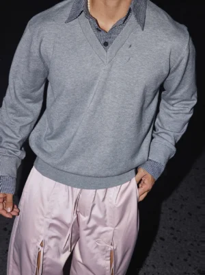 Heather gray Korean streetwear V-neck knit sweater with ribbed neckline, subtle chest logo, layered checked shirt collar, and relaxed wide-leg pants styling