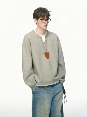 Heather gray men's layered crew neck sweatshirt in a front three-quarter studio view with white layered trim, wide-leg denim, and leather pendant styling