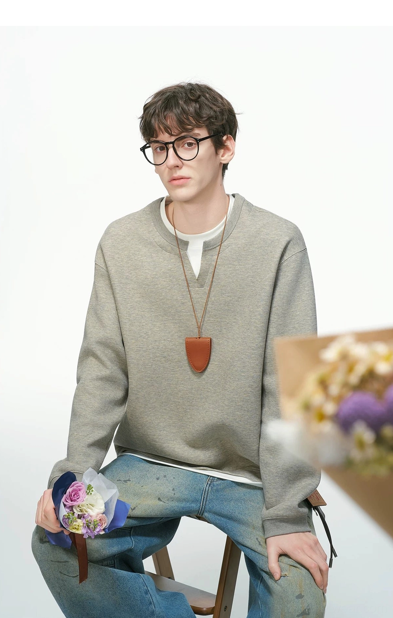 Heather gray men's layered crew neck sweatshirt worn seated with wide-leg denim, leather pendant necklace, and relaxed Korean street style
