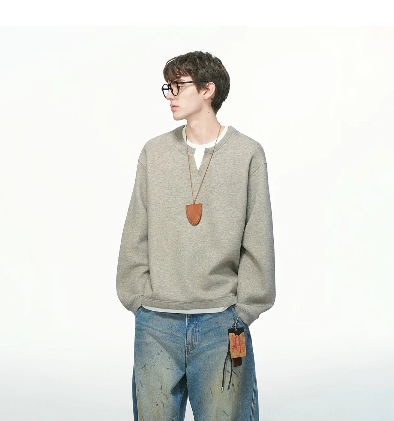 Left side profile of a heather gray men's relaxed layered crew sweatshirt styled with stained wide-leg denim and brown leather pendant