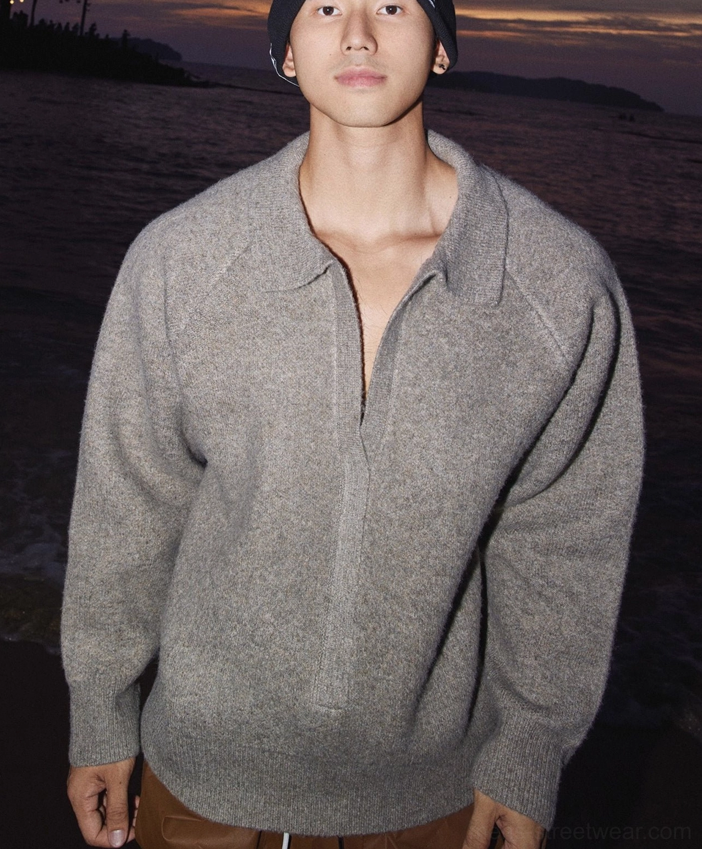 Heather gray oversized half-zip knit sweater with wide collar worn by male model with brown trousers and black beanie in seaside sunset streetwear look