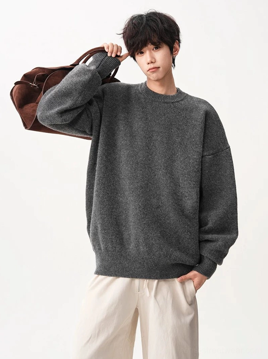 Three-quarter styling view of a heather gray oversized textured knit sweater with dropped shoulders and a brown suede shoulder bag