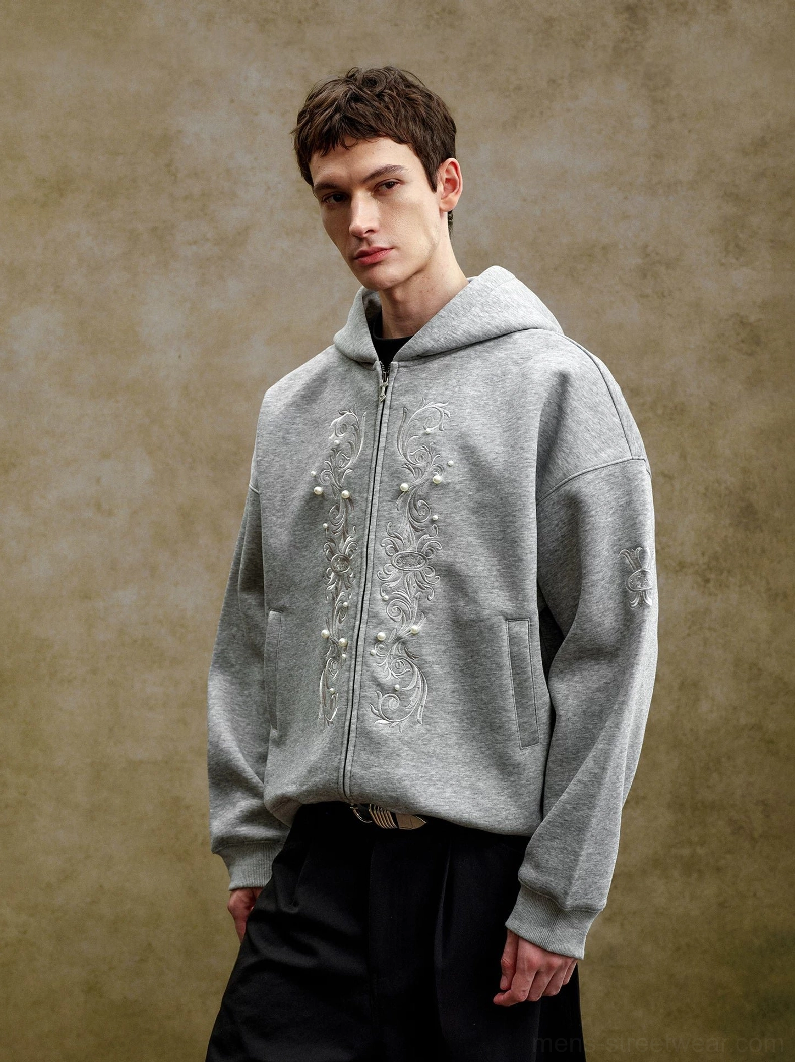 Heather gray pearl embroidered zip-up streetwear hoodie on male model showing relaxed boxy silhouette and ornate front motif