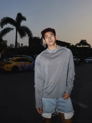 Front view of a male model wearing a light gray heathered raglan long sleeve tee in a relaxed Korean streetwear silhouette at dusk