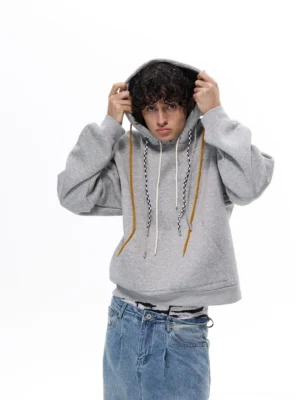 Heather gray oversized tri-cord drawstring hoodie shown from the front with a kangaroo pocket, loose fit, and contrasting mustard cream and braided black-white hood cords