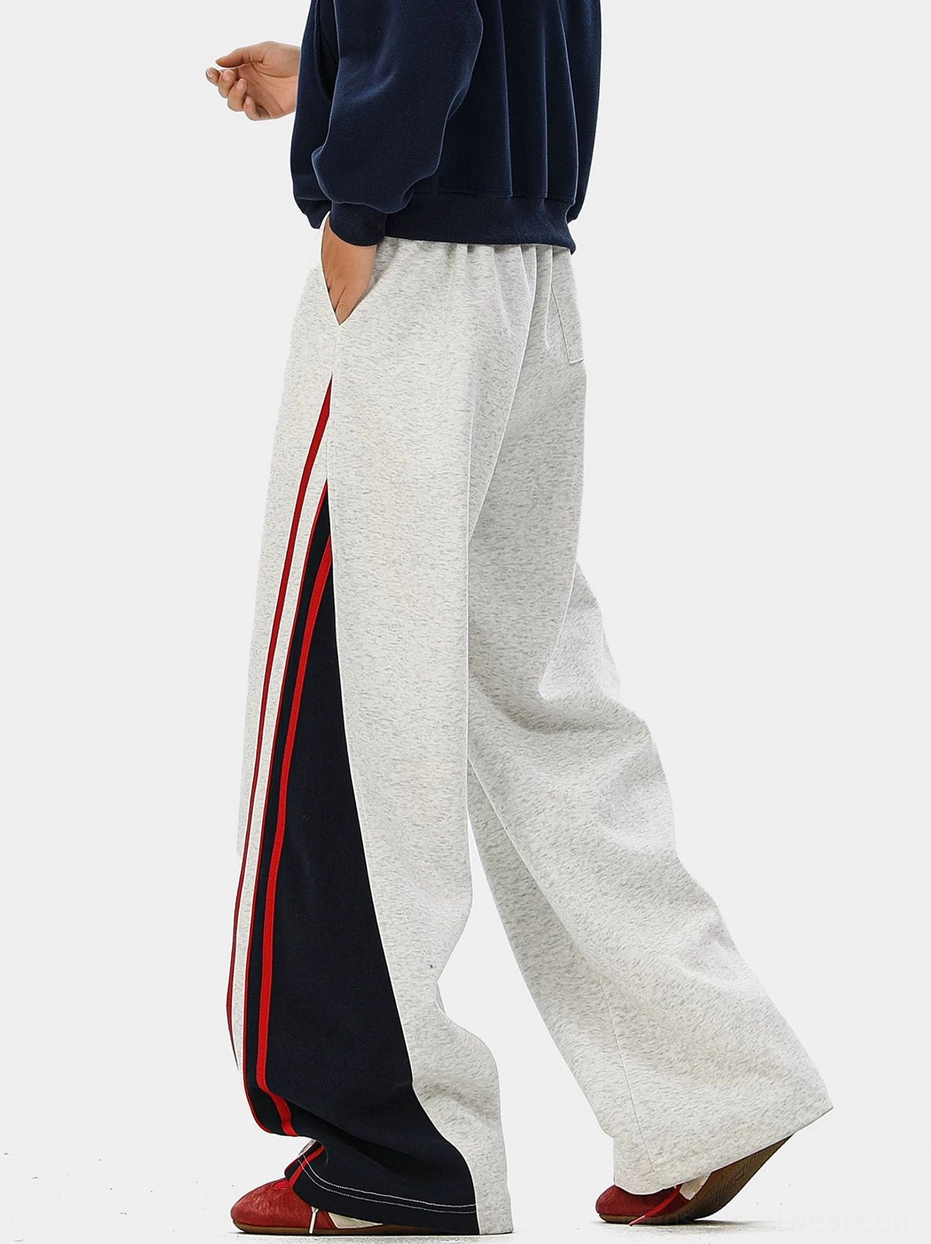 Side-back view of heather gray wide-leg varsity track pants with navy side panel, red stripe details, and drawstring waistband