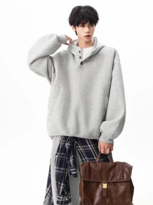 Heather grey oversized Henley hooded sweatshirt styled with a plaid shirt tied at the waist, wide-leg trousers, and a brown tote bag