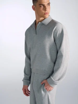 Heather grey oversized polo sweatshirt with open collar, dropped shoulders, wide sleeves, and matching wide-leg sweatpants in a minimalist streetwear studio outfit