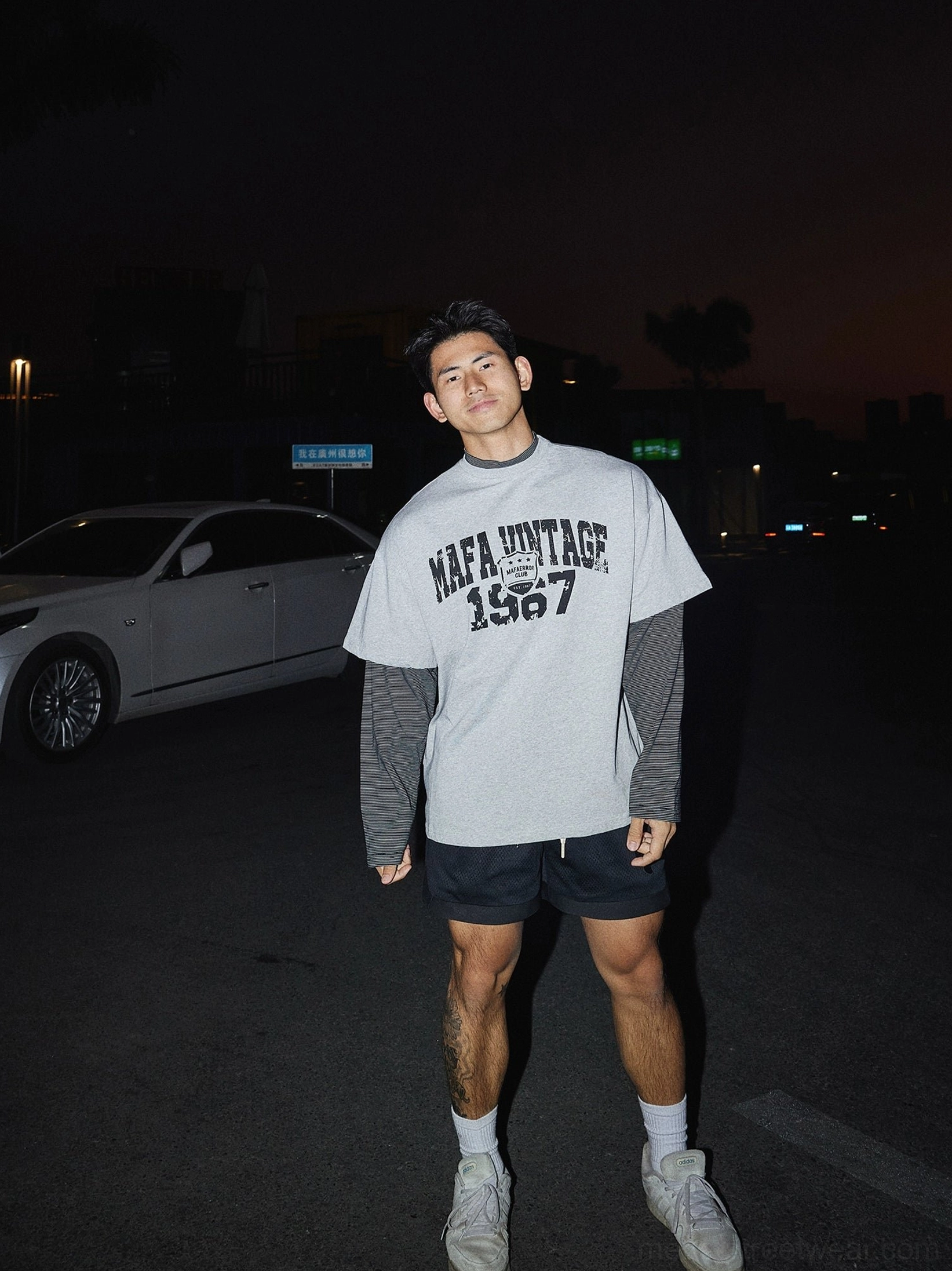 Full body view of heather grey oversized vintage graphic tee with layered sleeves styled with black shorts white socks and sneakers