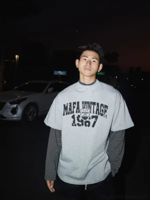 Heather grey oversized vintage graphic layered tee with distressed varsity print and attached contrast sleeves styled on a male streetwear model