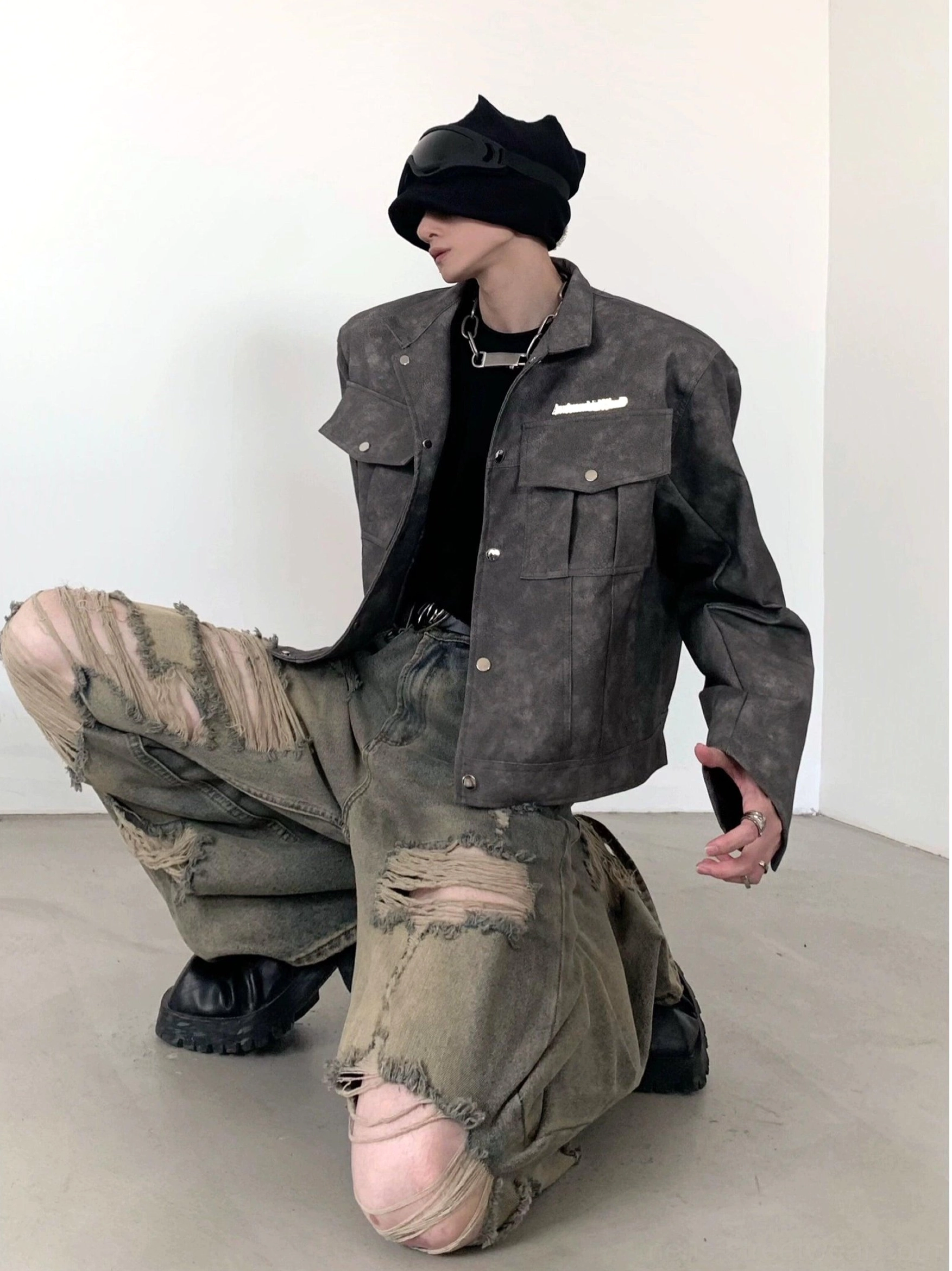 Side kneeling view of heavily distressed wide-leg denim cargo pants with large frayed knee and thigh rips