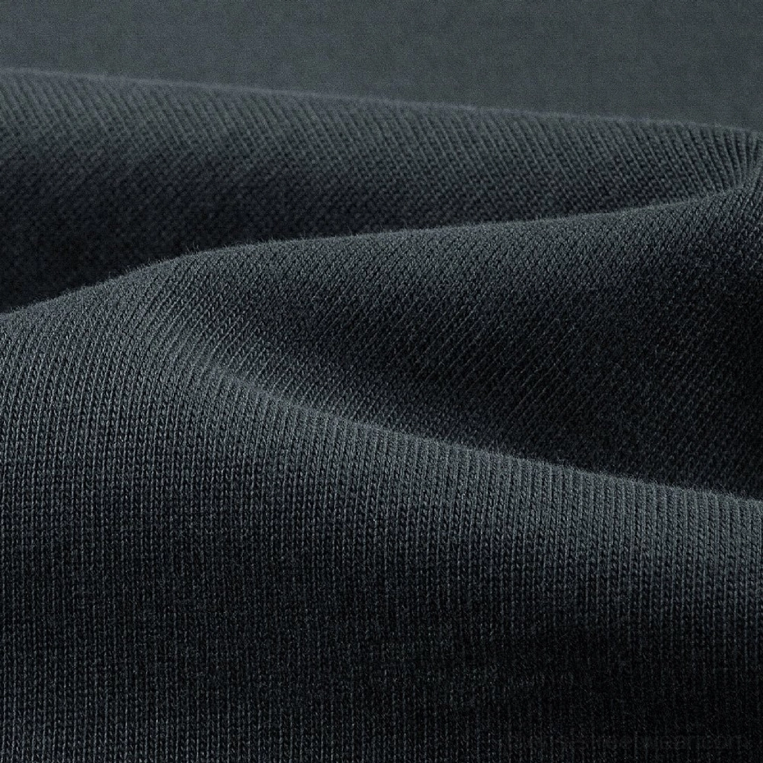 Close-up macro view of dense heavyweight cotton knit fabric texture on a dark gray oversized streetwear long sleeve tee
