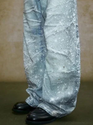 Close-up low angle view of heavyweight crystal embellished wide leg jeans with bleached wrinkle texture, sparkling rhinestones, and relaxed oversized denim hem