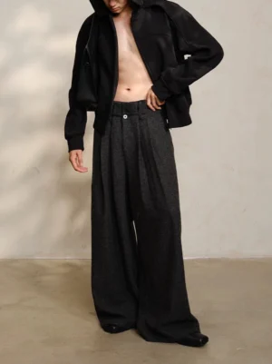 Male model wearing dark gray high-waist wide-leg wool tweed trousers with cropped black outerwear in a minimalist studio