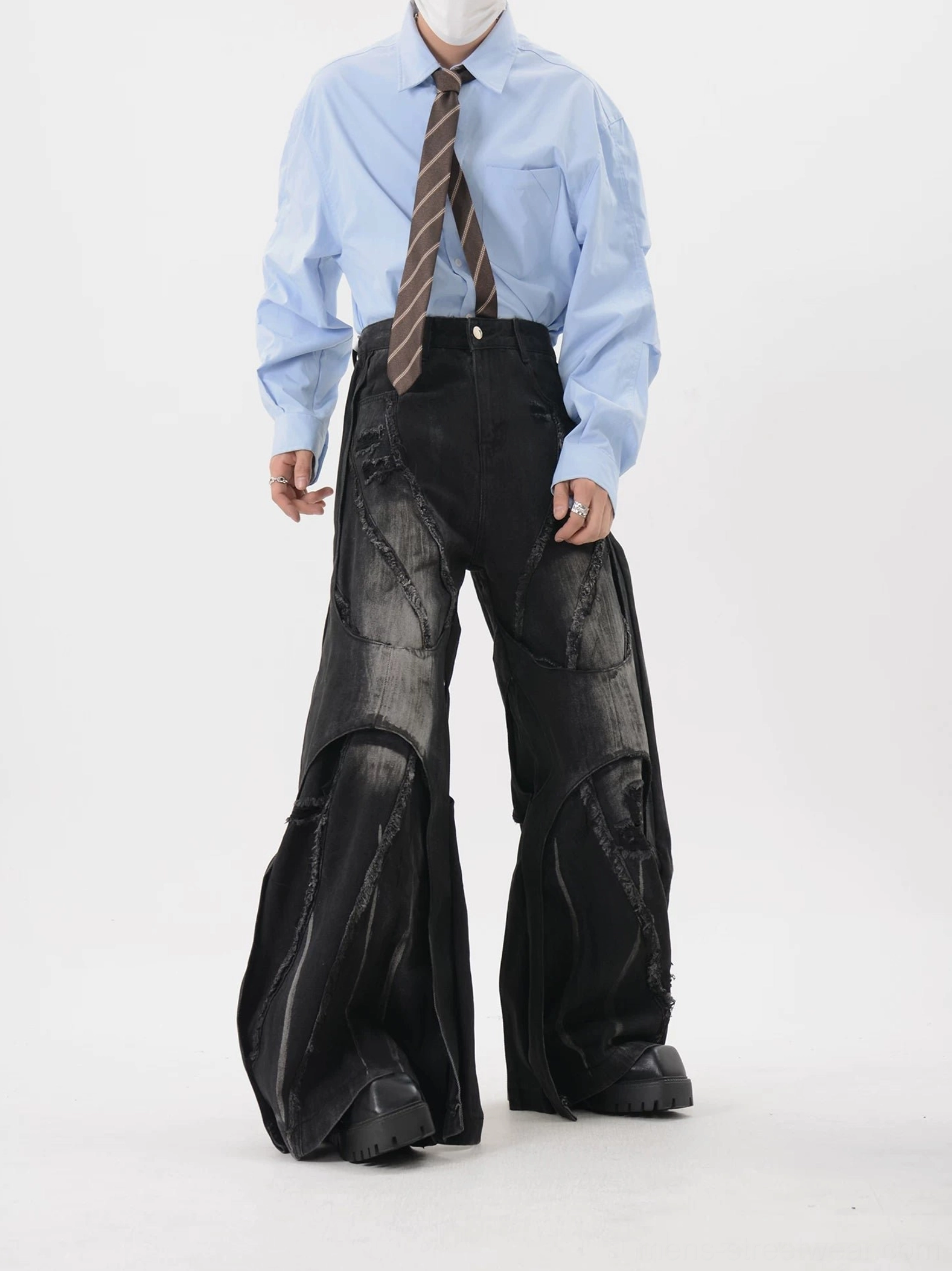 Full front view of high-waisted black deconstructed jeans showing raw frayed seams, distressed knee panels, button fly, and ultra-wide legs
