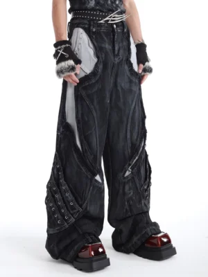 Three-quarter view of high-waisted black wide-leg jeans with asymmetric grey panels, industrial rivet accents, and relaxed Korean streetwear styling