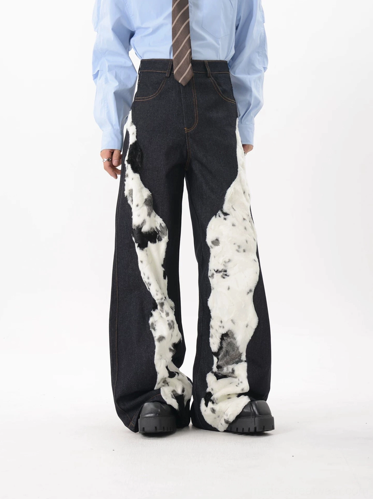 Side front view of high waisted cow print spliced denim trousers with contrasting fuzzy faux fur details and wide legs