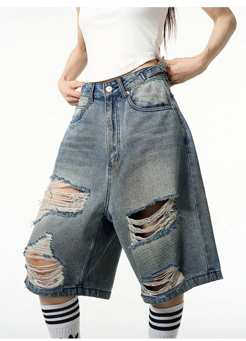Close-up front view of high-waisted oversized distressed denim Bermuda shorts with vintage faded blue wash and large thigh rips
