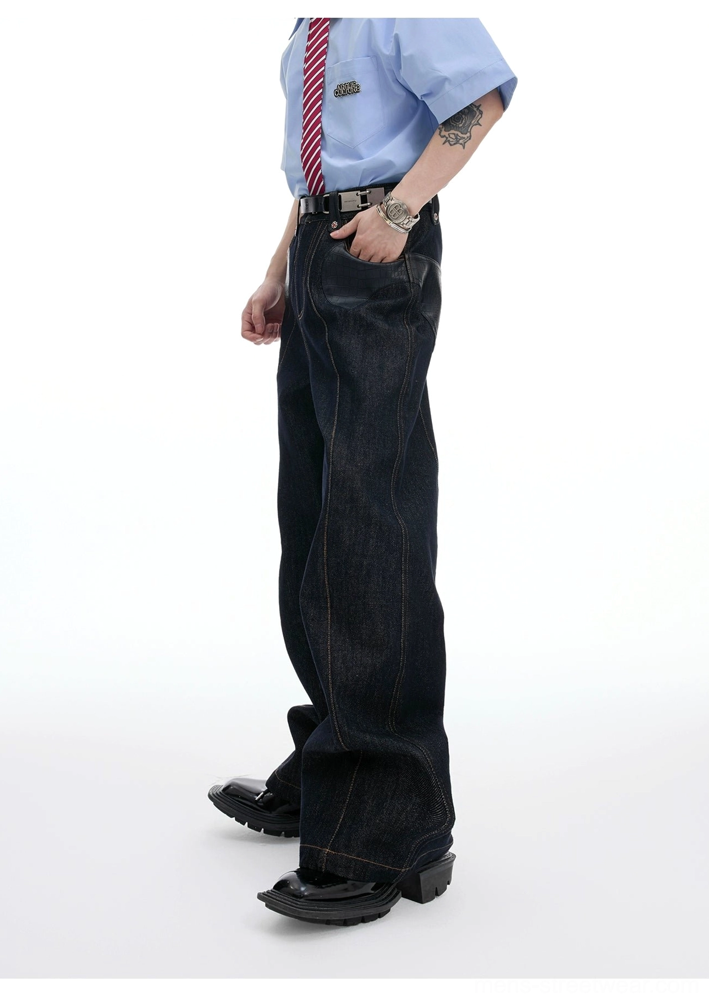 Side view of a male model wearing high-waisted wide-leg dark indigo denim pants with a leather belt and coordinated streetwear accessories