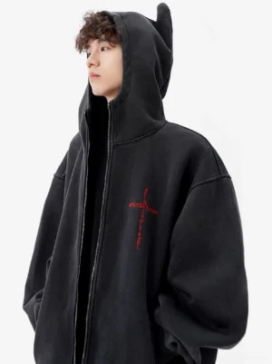 Washed black horned oversized zip hoodie shown in left side profile with pointed hood, red gothic cross embroidery, drop shoulders, and relaxed streetwear fit