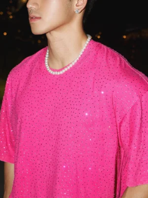 Close-up of a hot pink oversized rhinestone T-shirt showing the crew neck loose drop shoulders and sparkling embellishments