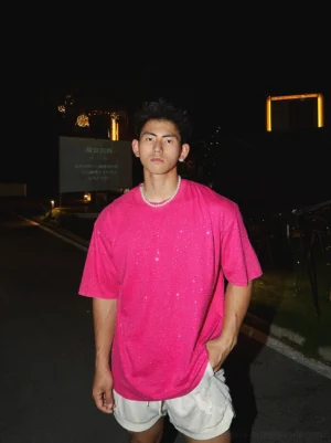 Hot pink oversized rhinestone T-shirt styled with white casual shorts in a nighttime streetwear setting