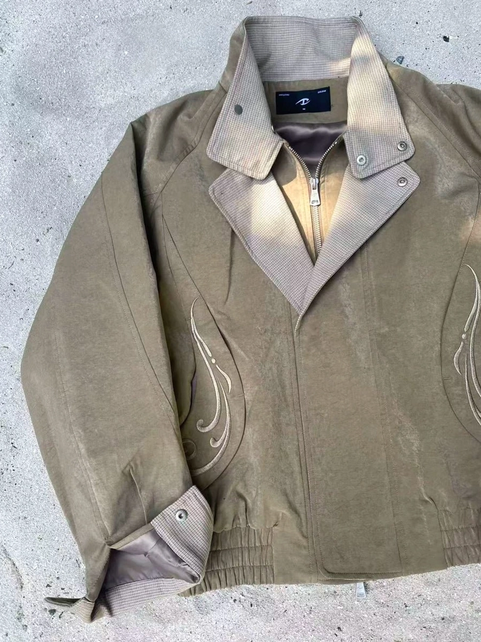 Close-up view of cropped streetwear bomber jacket with houndstooth layered collar, flame chest embroidery, snap fasteners, and adjustable cuffs