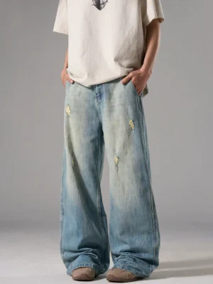 Three-quarter front view of faded vintage blue baggy jeans showing diamond distressing, whiskering, pockets, and wide-leg construction