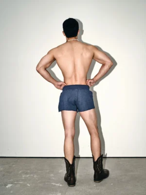 Back view of dark indigo Korean streetwear sweat shorts with short athletic silhouette and elastic waistband styled with cowboy boots