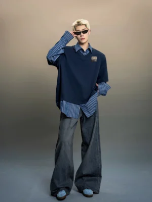 Full body view of an oversized indigo layered stripe fake two-piece streetwear shirt top with blue vertical stripes, exposed shirt hem, and metal chest patch