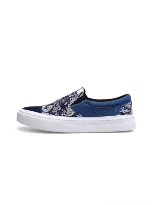 Side profile of indigo blue paisley patchwork slip-on sneakers with denim canvas panels, elastic side inserts, and white rubber sole