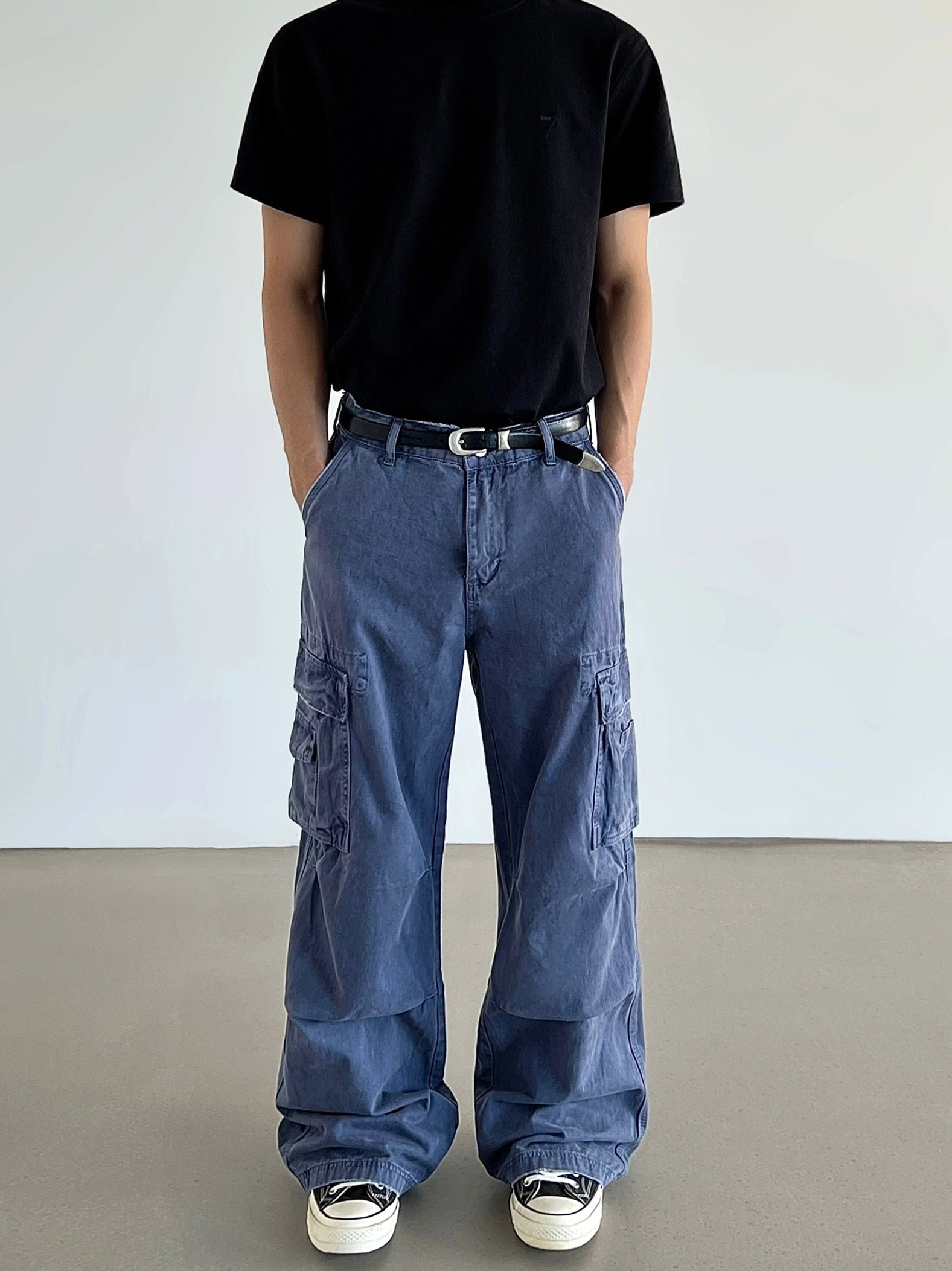 Front three-quarter view of indigo washed utility cargo pants showing relaxed draped wide-leg fit and flap cargo pockets