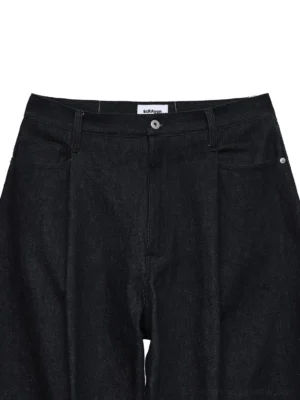 Close-up of dark indigo wide-leg jeans waist with button fly, belt loop, woven waistband label, front pocket, and metal rivet
