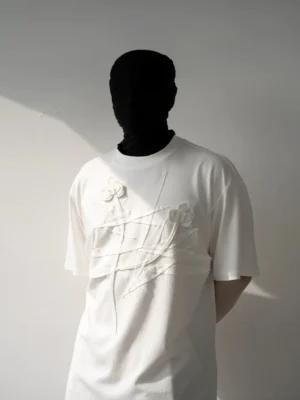 Close-up front view of an ivory 3D floral relief T-shirt with crossed fabric appliqué details on the chest, relaxed Korean streetwear fit, and sculptural textured artwork