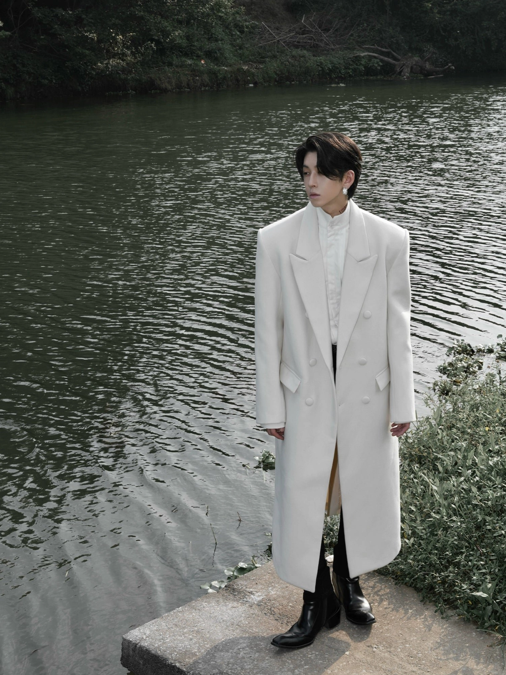 Men's ivory ankle-length double-breasted wool blend overcoat styled with black leather boots in an outdoor city setting
