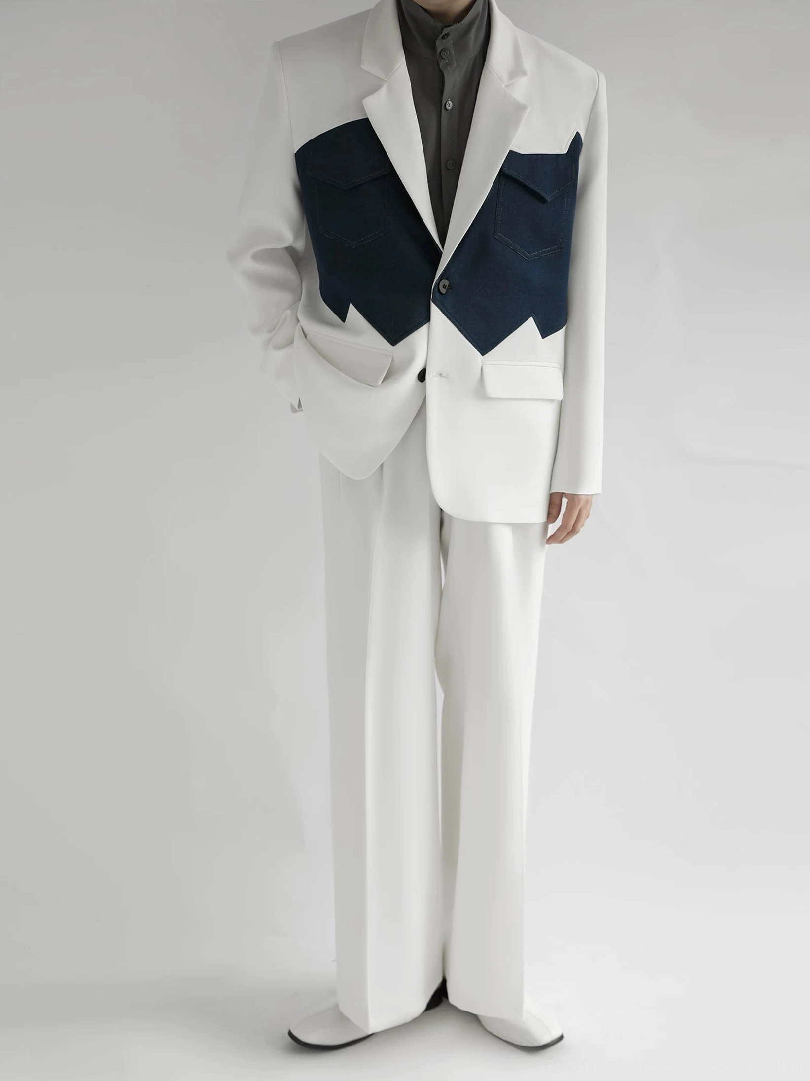 Full-body view of a relaxed ivory Western-inspired suit with dark navy contrast pocket panels and wide-leg tailored trousers