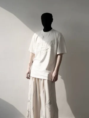 Full-body front view of an oversized ivory floral relief T-shirt styled with printed wide-leg pants, showcasing Korean streetwear proportions and raised chest artwork