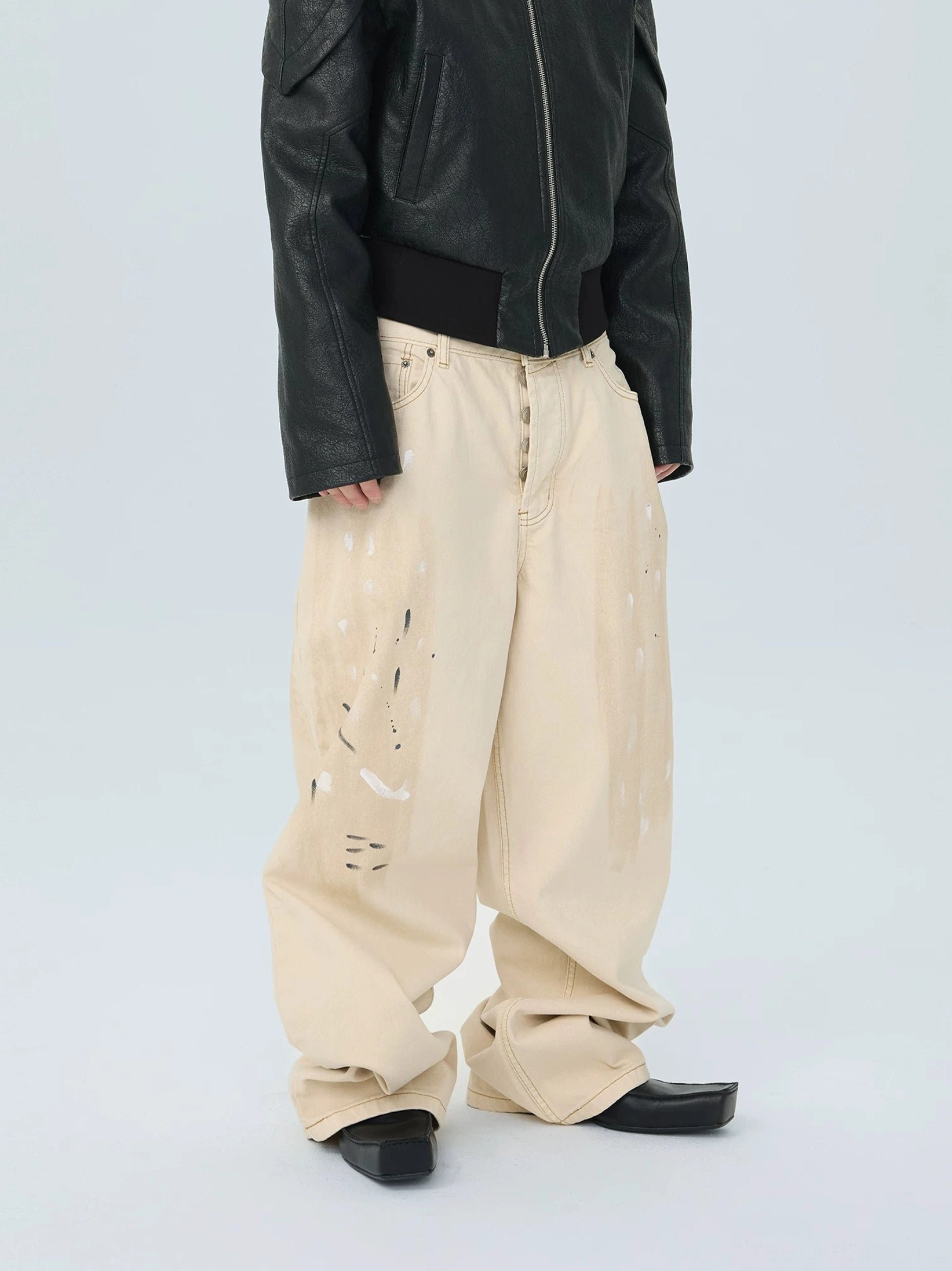 Side front view of ivory paint splatter baggy jeans with long stacked hems and oversized streetwear fit