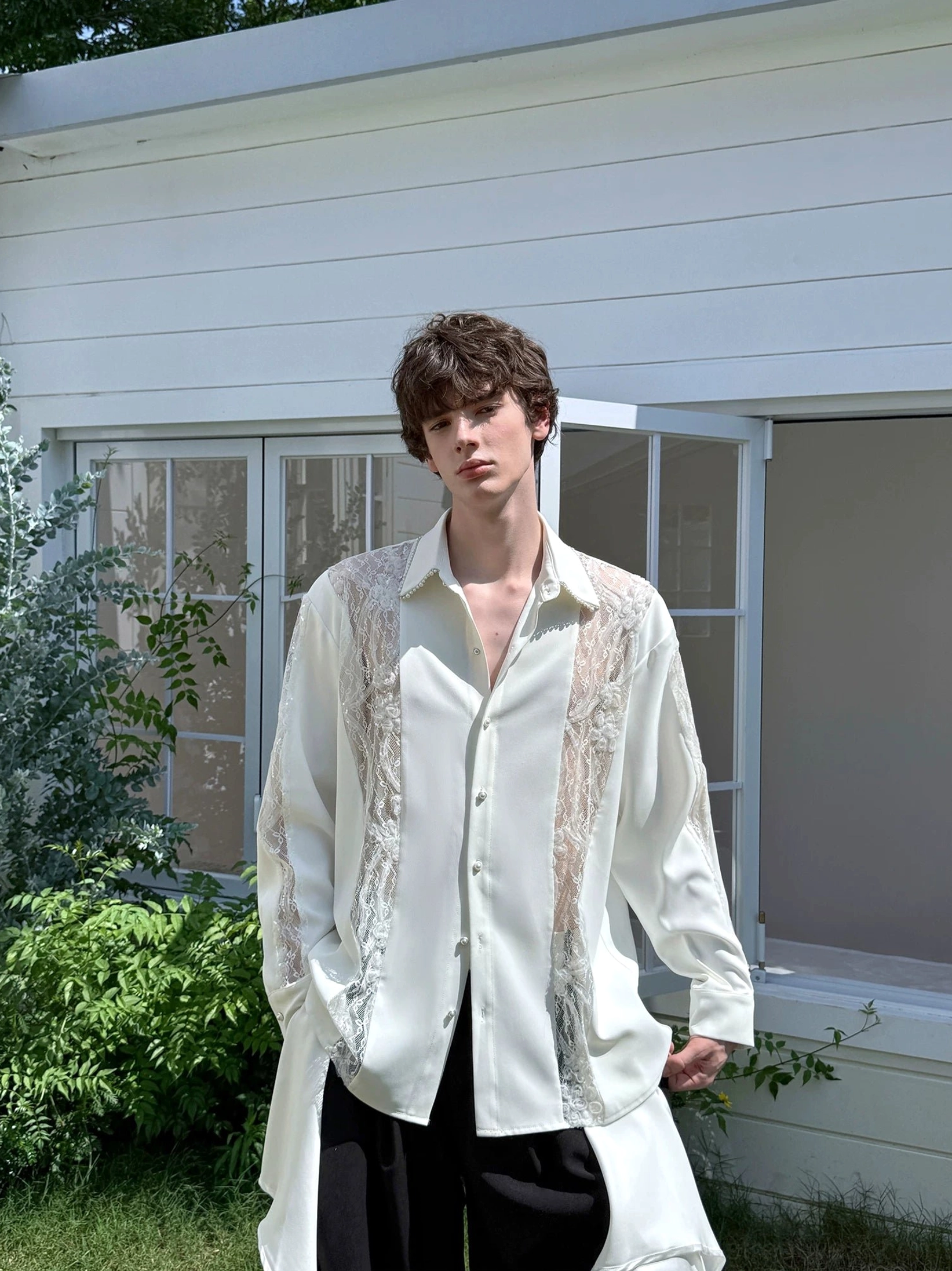 Men's ivory lace panel longline button-down shirt styled with black wide-leg pants in an outdoor streetwear look